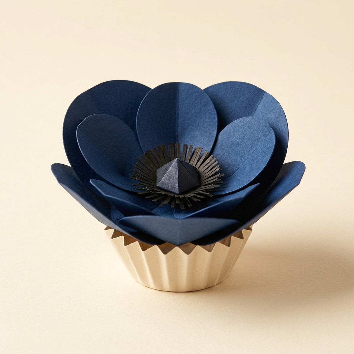 Anemone paper flower in indigo on its pleated paper cup, packshot on cream