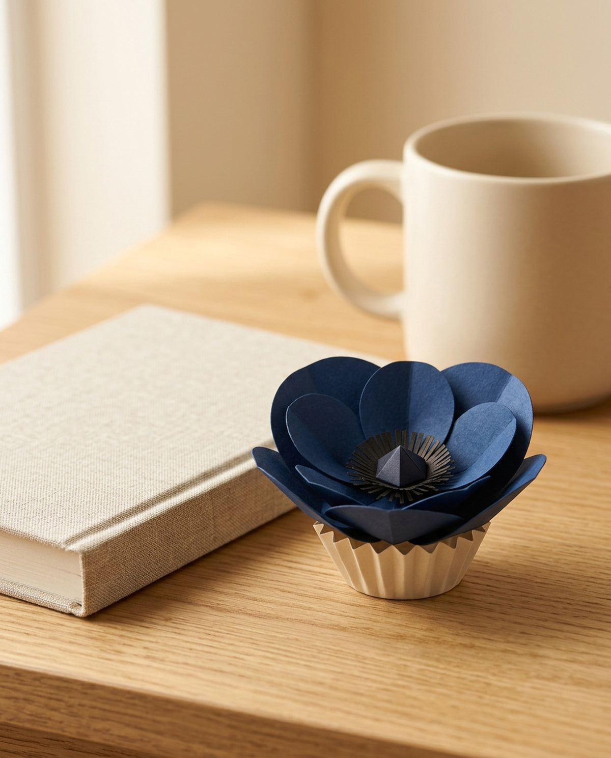 [CONCEPT PLACEHOLDER] Anemone paper flower in indigo on its pleated paper cup, on a desk with a book and a mug (AI concept image, not the final product)