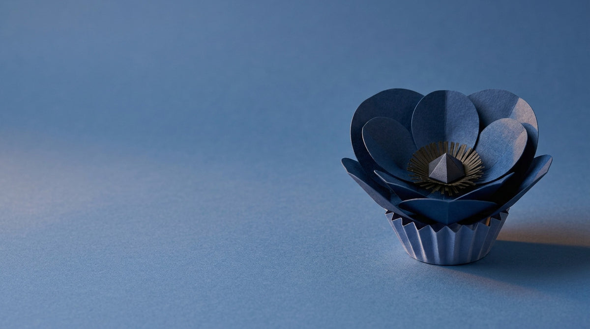 [CONCEPT PLACEHOLDER] Anemone paper flower in indigo on its pleated paper cup, colour moment on a tonal paper background (AI concept image, not the final product)