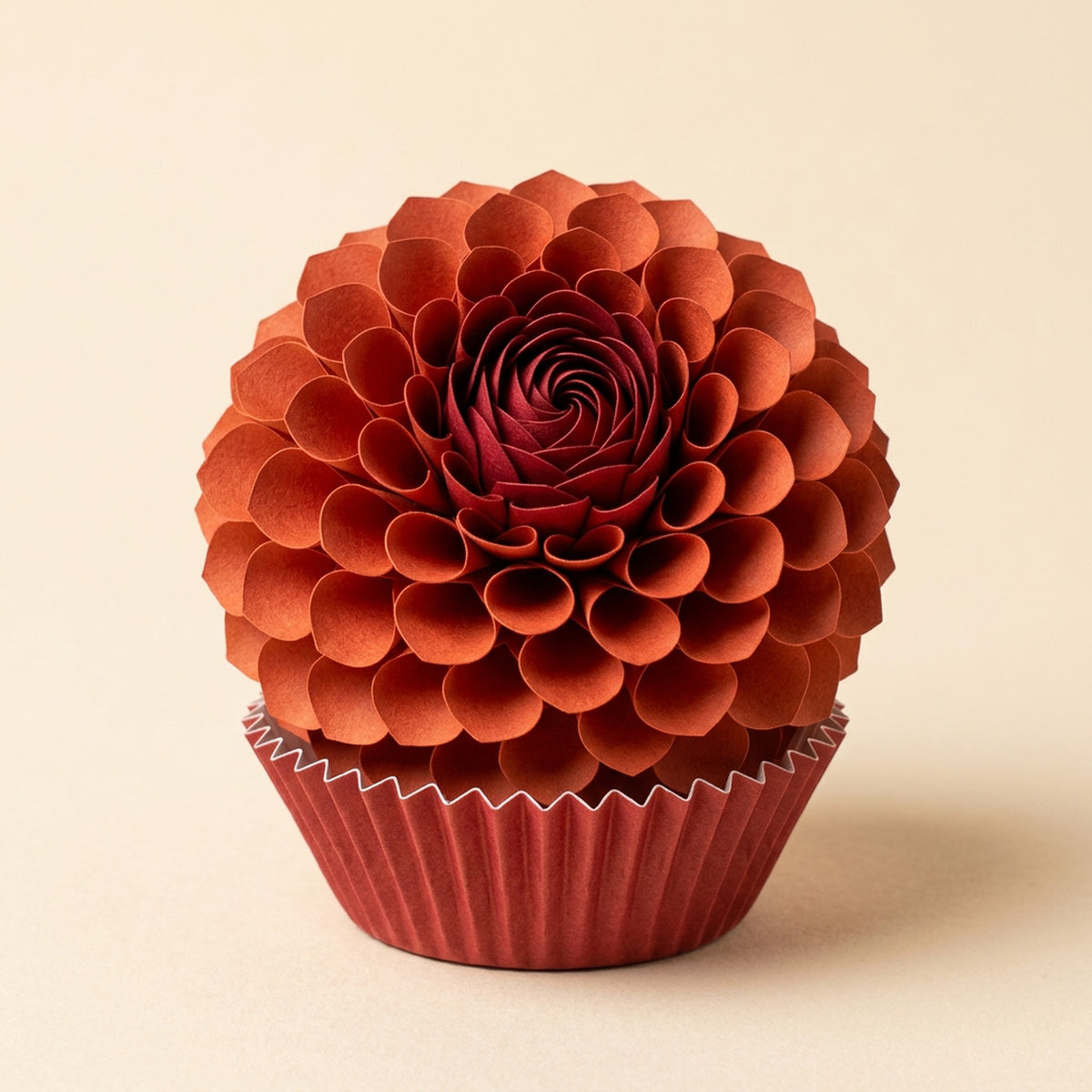 Dahlia paper flower in sumac red on its pleated paper cup, packshot on cream