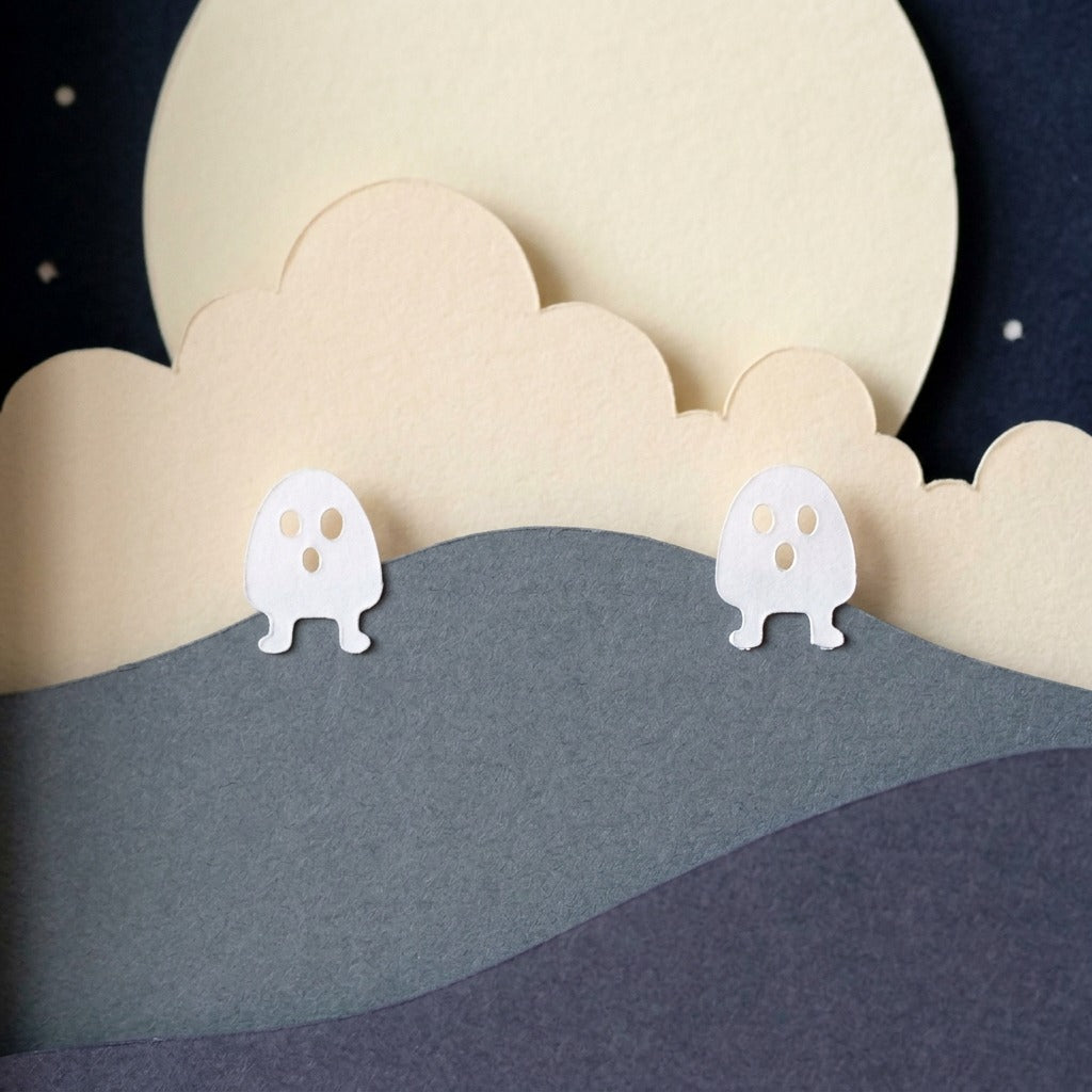 Close-up of two white paper spirits on the night hills below the cloud and moon